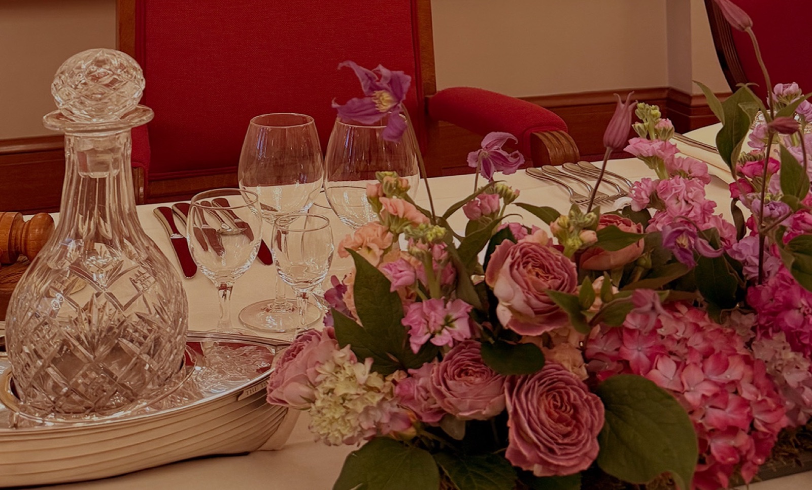 Pink roses, hydrangea and stocks beside a crystal decanter on a banquet table